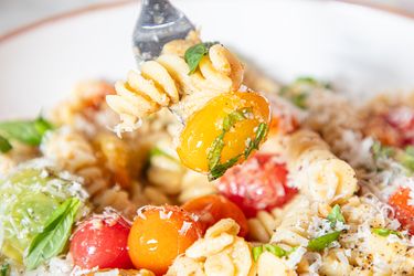 Dish of pasta garnished with tomatoes basil and grated cheese with a fork lifting a bite