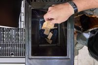 A person places wood chips into the Masterbuilt Gravity Series 1150 Digital Charcoal Grill and Smoker