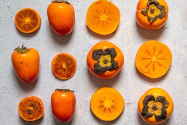 A variety of persimmons, some cut and some whole, arranged in a grid on a stone surface