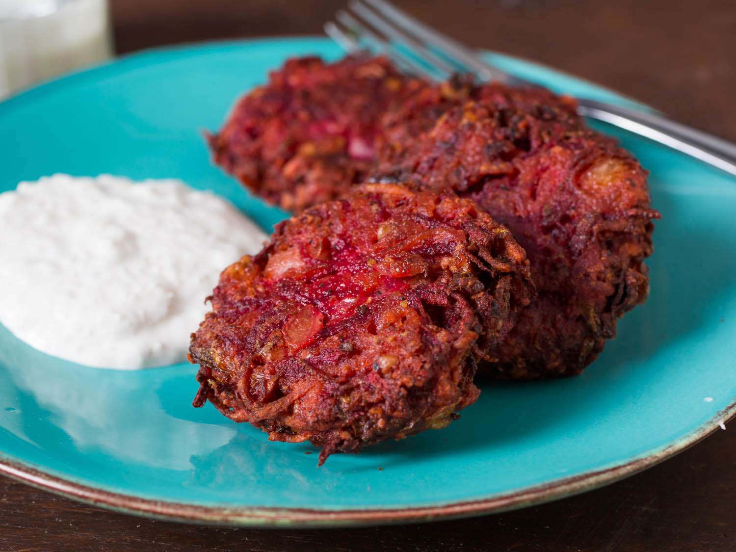 Close-up of beet latkes on a blue plate, next to a dollop of sour cream