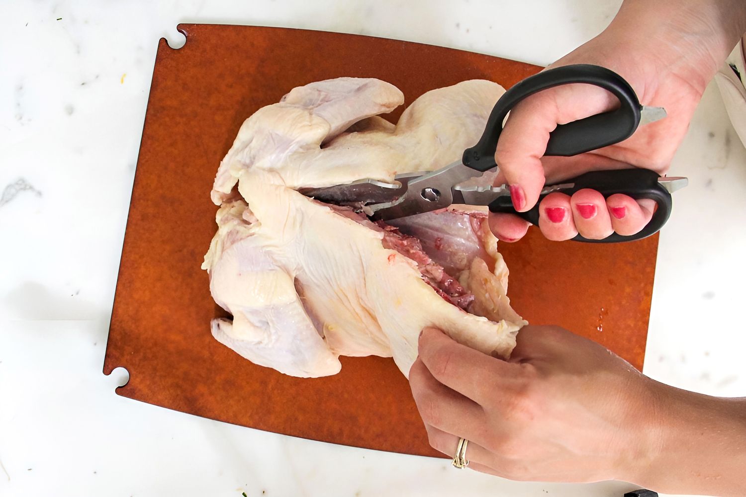 Hands using kitchen shears to cut a raw chicken on a cutting board