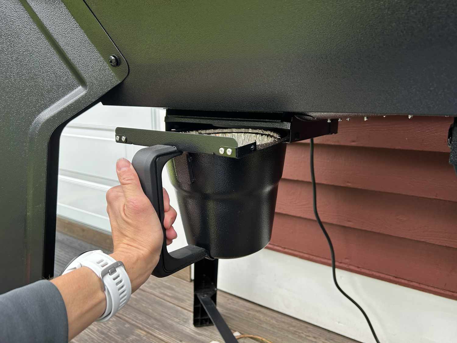 A person pulling out the grease trap of the Traeger Woodridge pellet grill