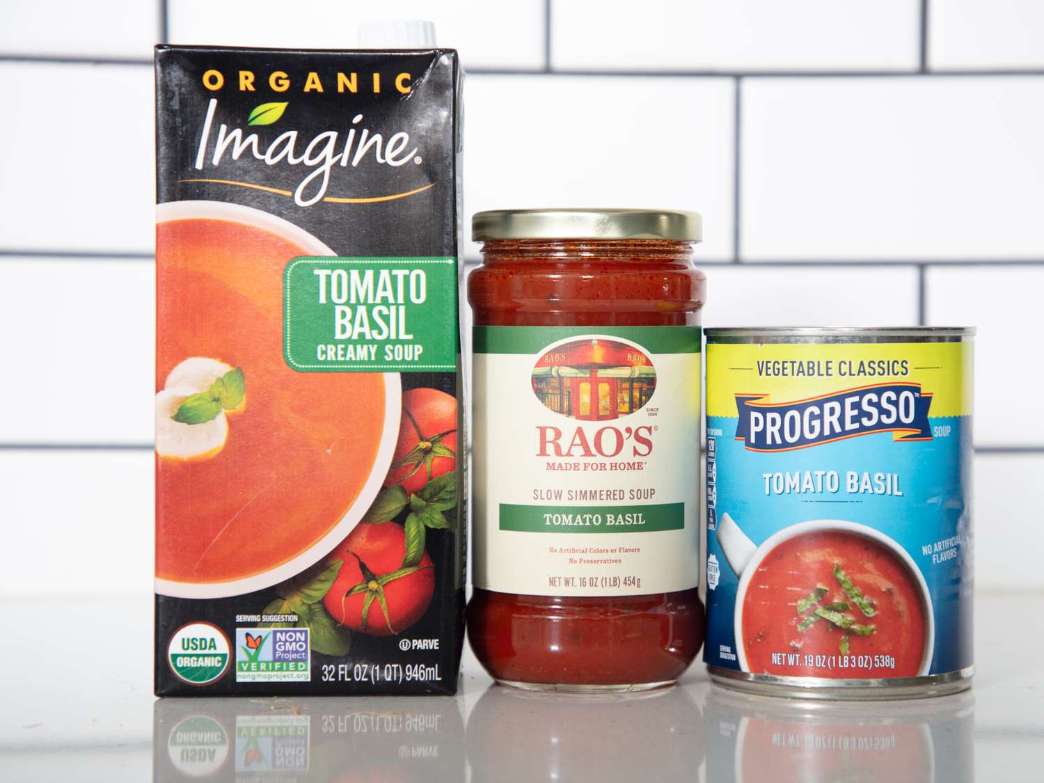 Three tomato basil soups from different brands Imagine carton Raos jar and Progresso can displayed side by side on a counter