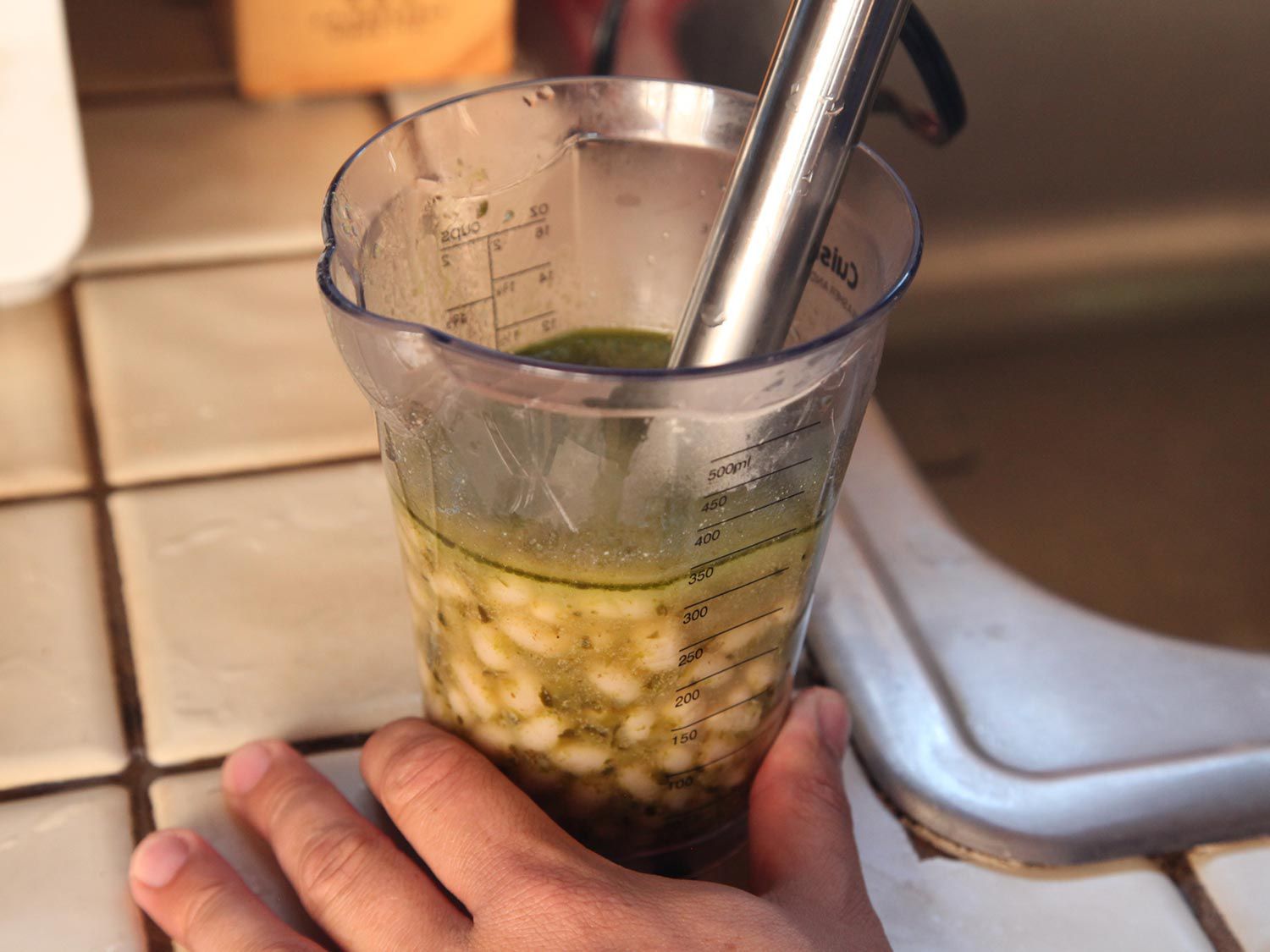 An immersion blender pureeing white beans in the green chile liquid.
