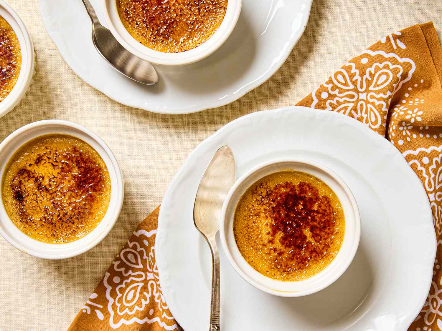 Pumpkin crme brle desserts with caramelized tops served in small ramekins with spoons on plates