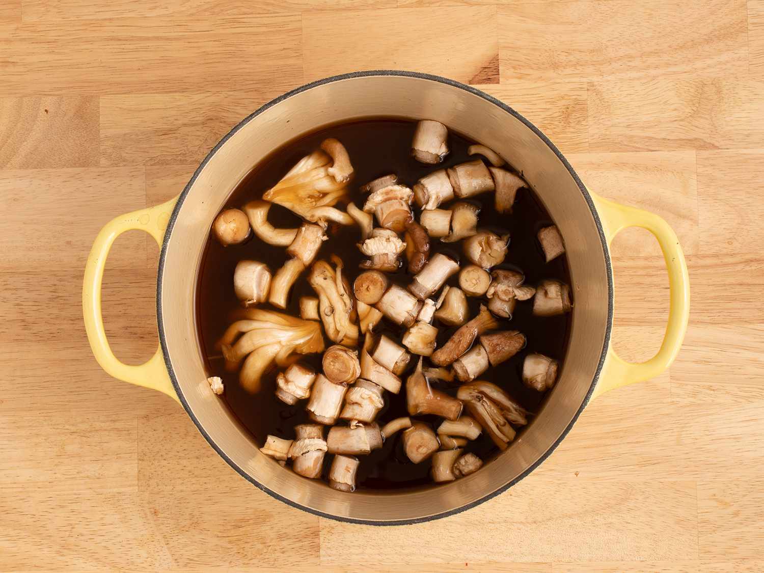 Mushrooms and stock in a dutch oven on a wooden counter.