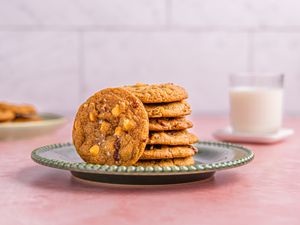 A plate of cookies with visible nuts, with a glass of milk in the background