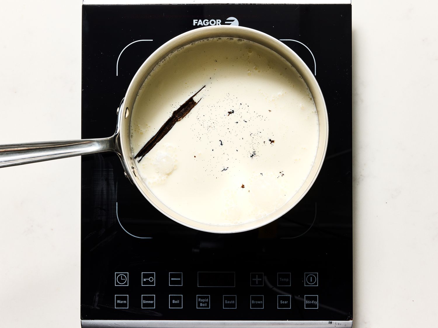 Custard mixture with vanilla bean in pot on induction stove