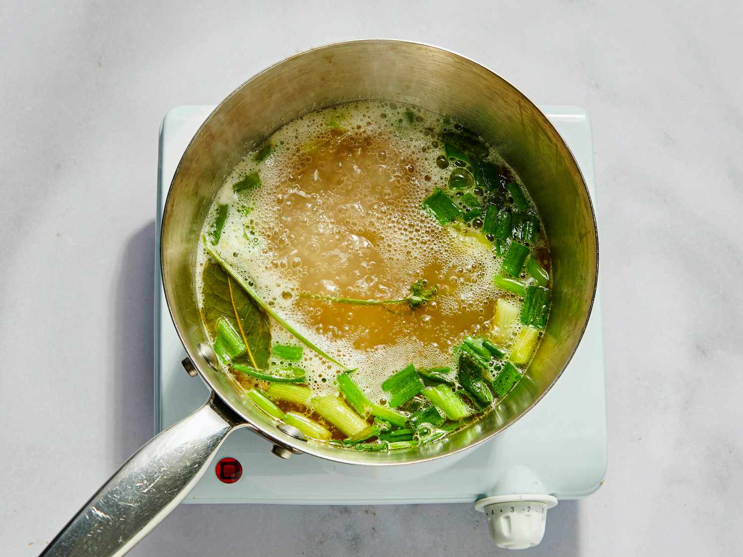 chicken broth, green onion, cilantro, bay leaf, 4 garlic cloves simmering in small saucepan