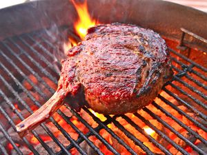 A large bone-in ribeye steak grilling on a charcoal grill.