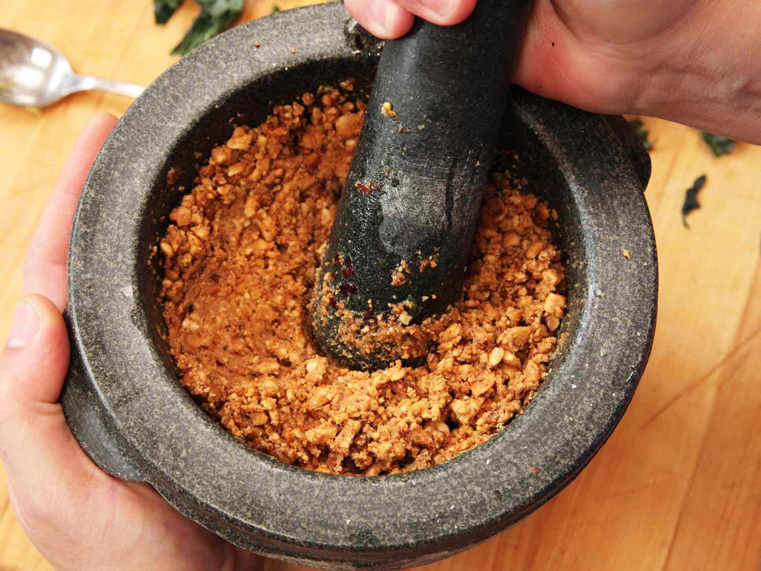 Pounding toasted peanut with mortar and pestle.