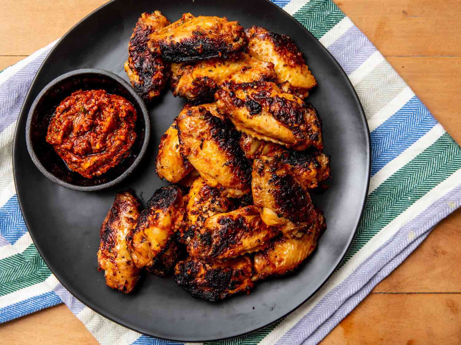 Overhead shot of a plate of grilled and charred Turkish-style chicken wings with a ramekin of spicy red pepper dipping sauce.