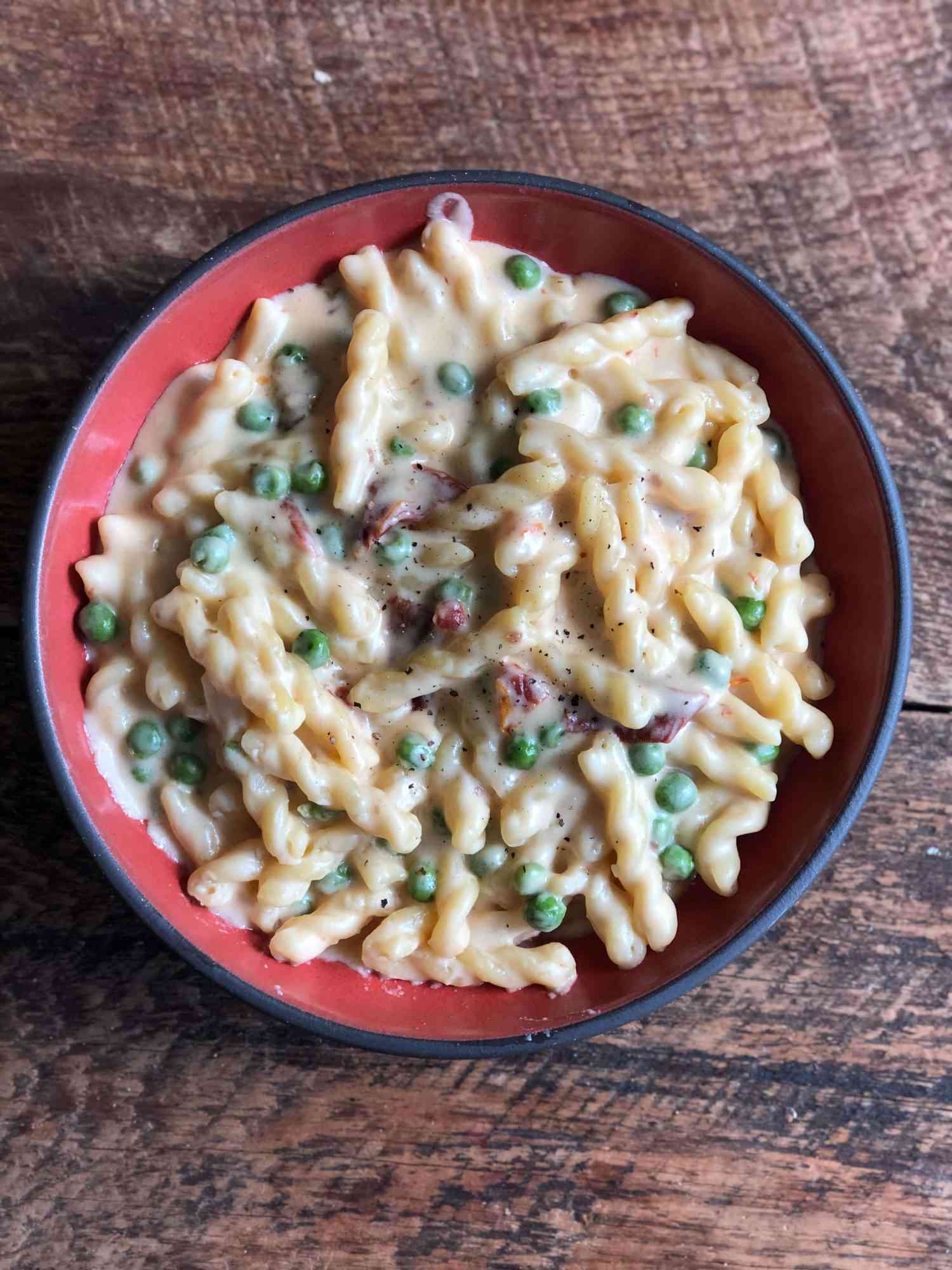 overhead view of a bowl of mac and cheese with peas and sun-dried tomatoes