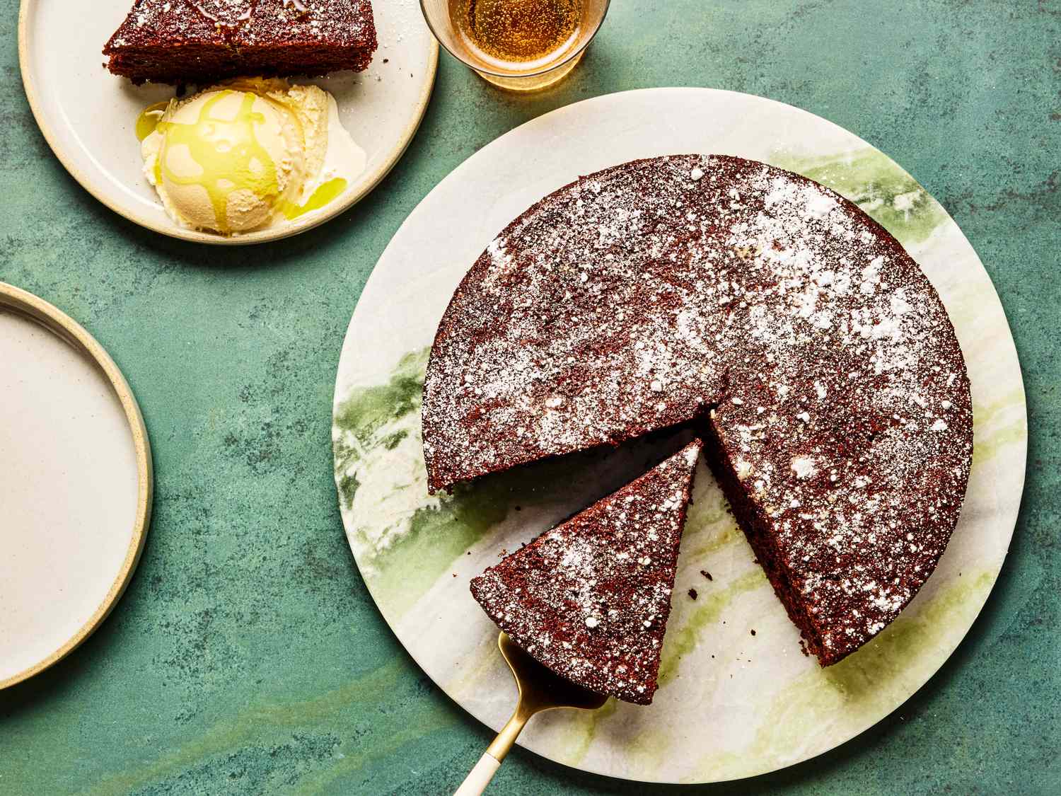 Chocolate olive oil cake sliced on a serving plate with a piece of cake accompanied by ice cream on a side plate
