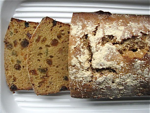 Overhead view of a freshly baked sticky malt loaf, served on a ridged platter. Two slices have been cut and shingled to reveal the interior texture of the quick bread.