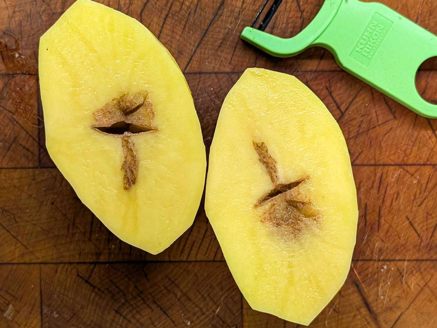 Two halves of a peeled potato with a peeler on a wooden surface showcasing the internal discoloration