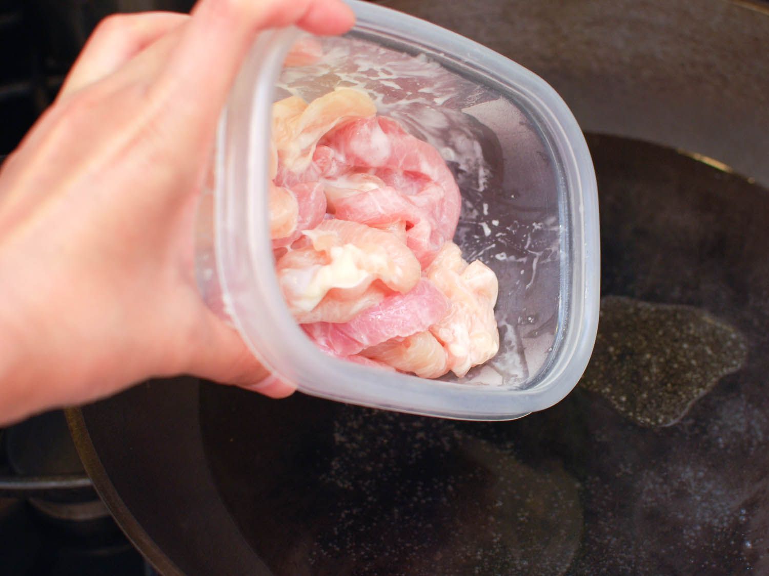 Marinated chicken and pork being poured into a wok.