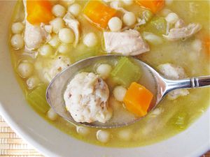 Overhead closeup of a spoon holding up a bite of homemade chickarina soup directly above the bowl.