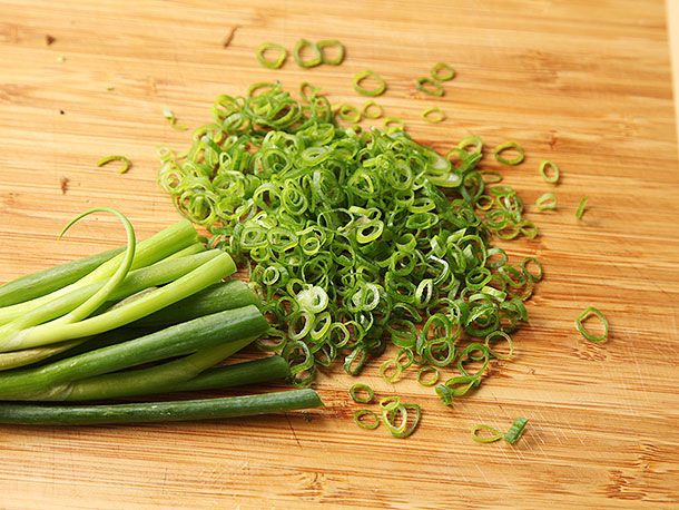 Scallions that have been cut into tiny slivers and are resting on a cutting board.