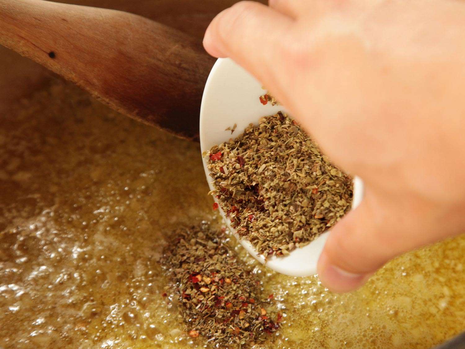 Adding dried oregano and red pepper flakes to hot garlic and olive oil