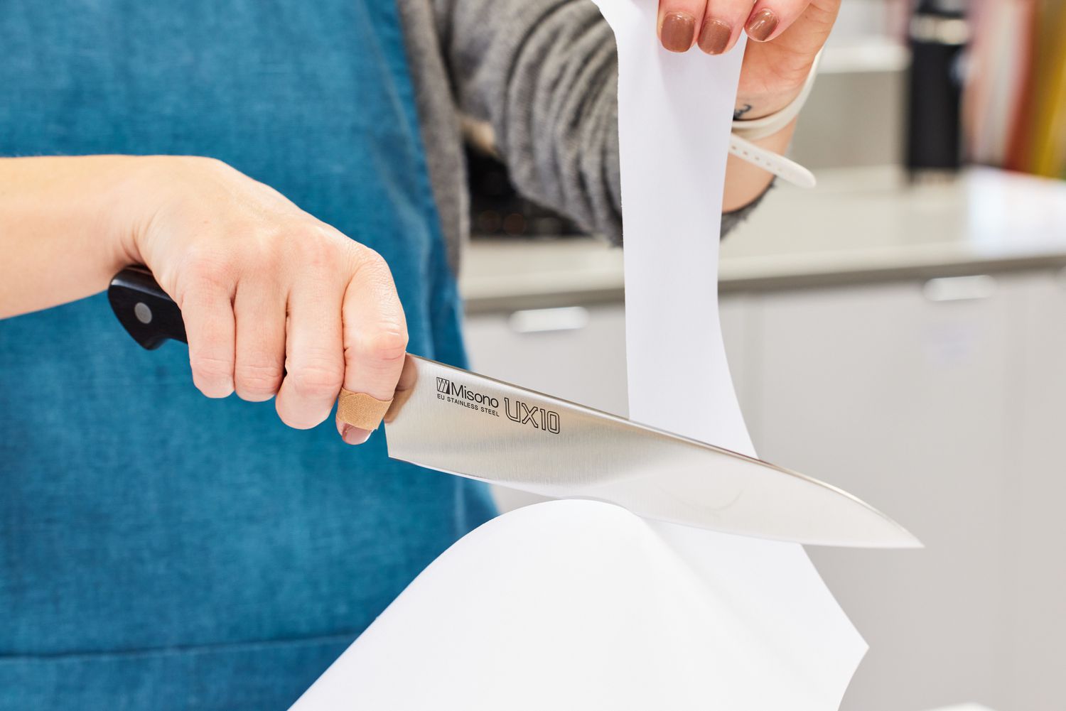 Hands slicing a piece of paper with a Misono UX10 8.2-Inch Gyutou