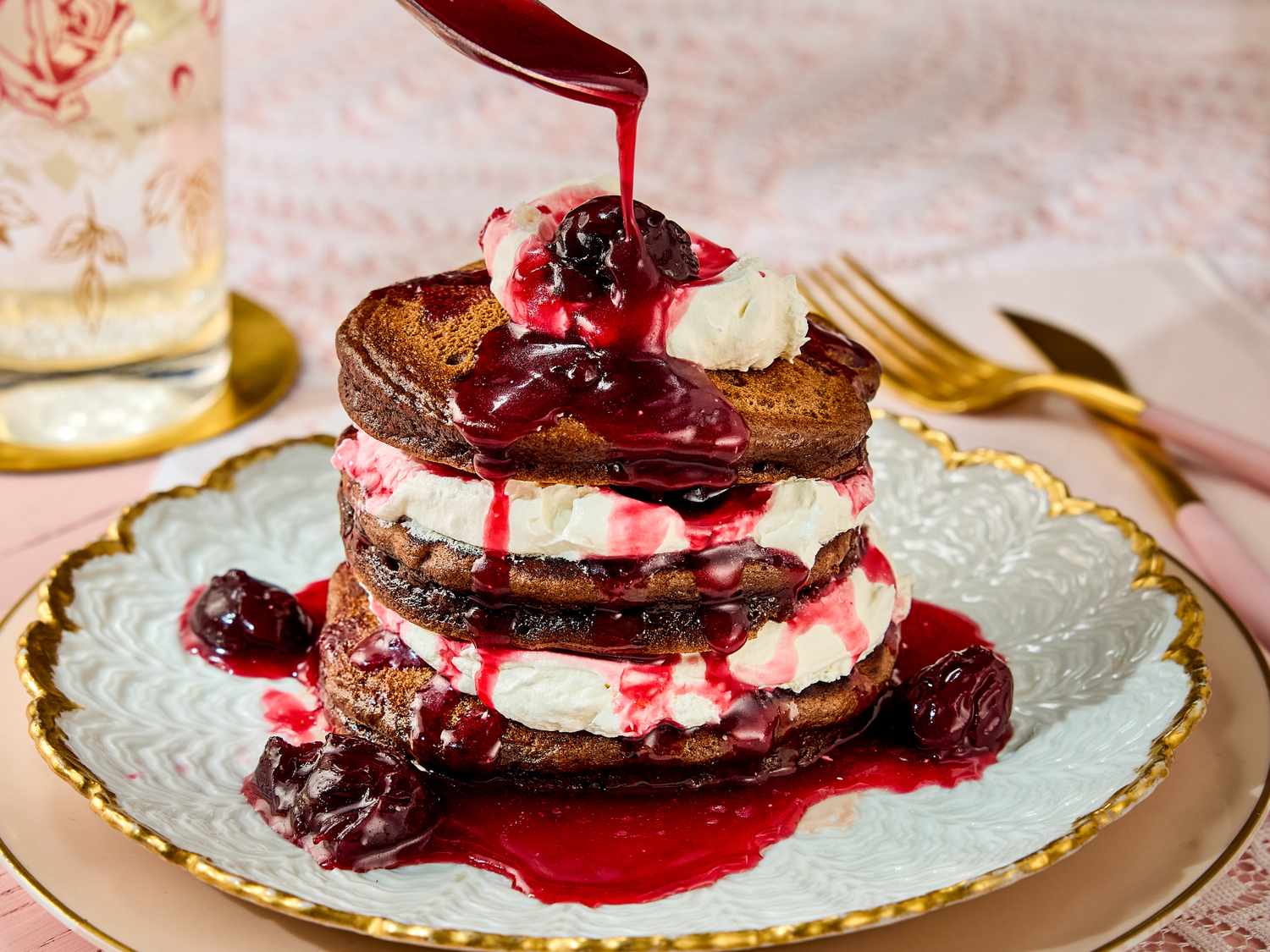 Stack of pancakes layered with cream and topped with berry sauce on a decorative plate