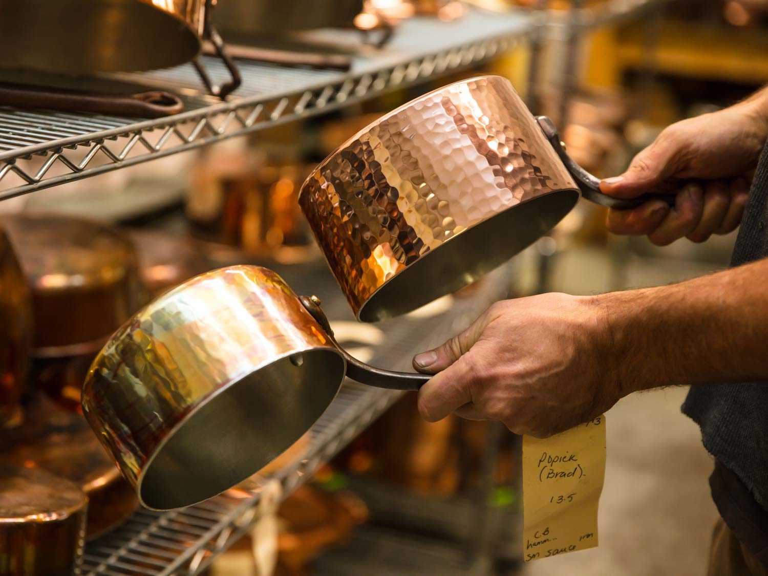 Hands holding hand hammered and spun copper saucepans.