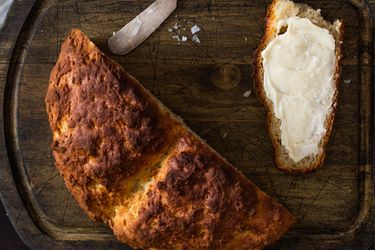 Overhead view of half crusty, golden brown Irish soda bread and buttered slice on wooden cutting board