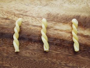 Three pieces of cooked gemelli pasta arranged in parallel on a wooden cutting board.
