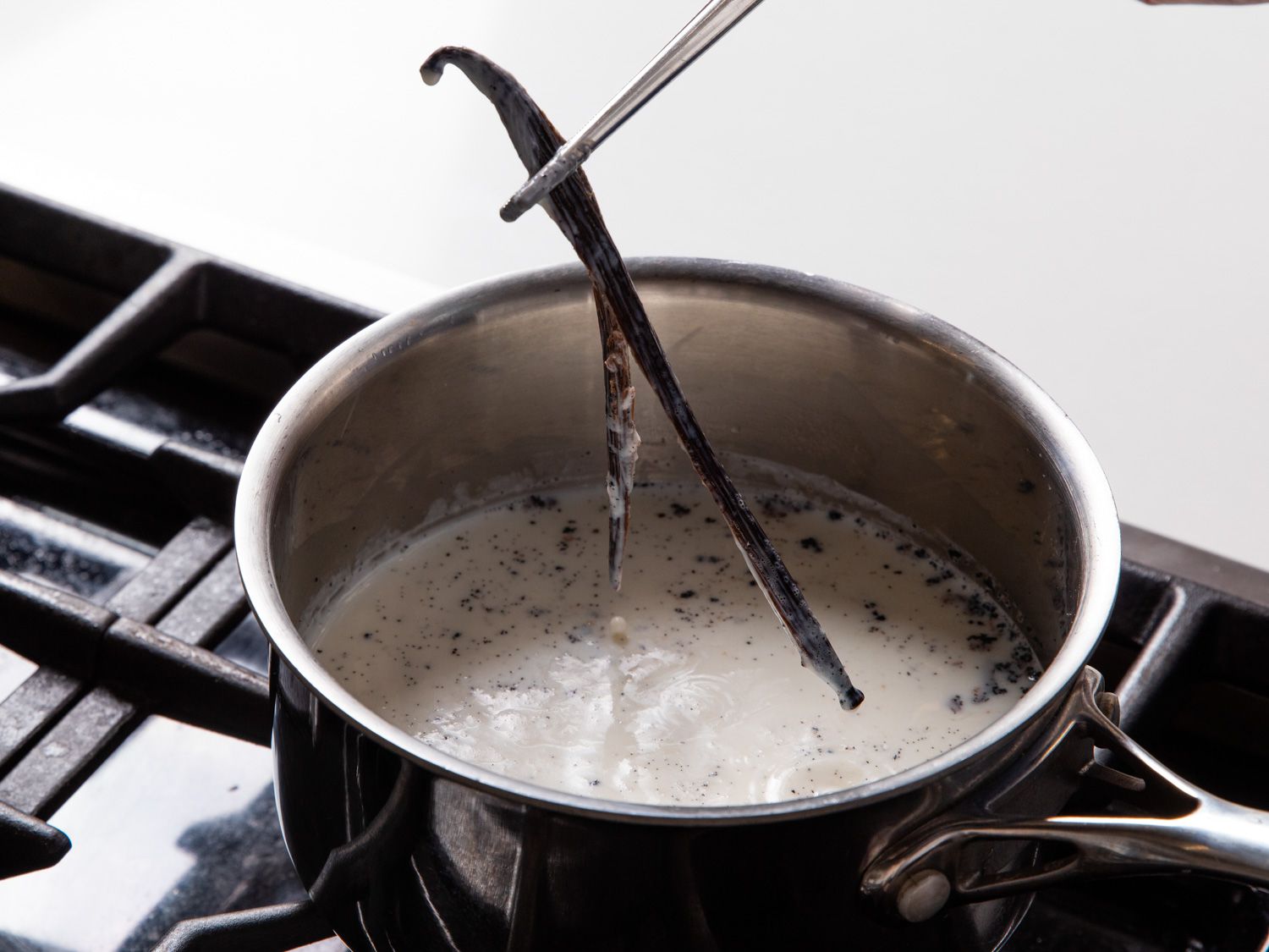 A vanilla bean being removed from a pot of milk after steeping.