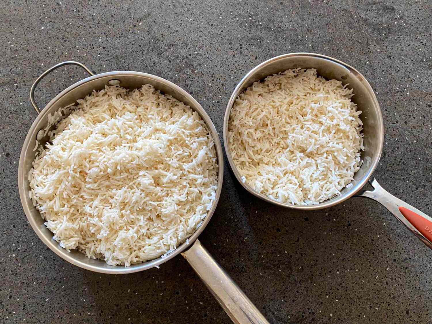 Two pots filled with cooked rice one large and one smaller placed on a dark surface