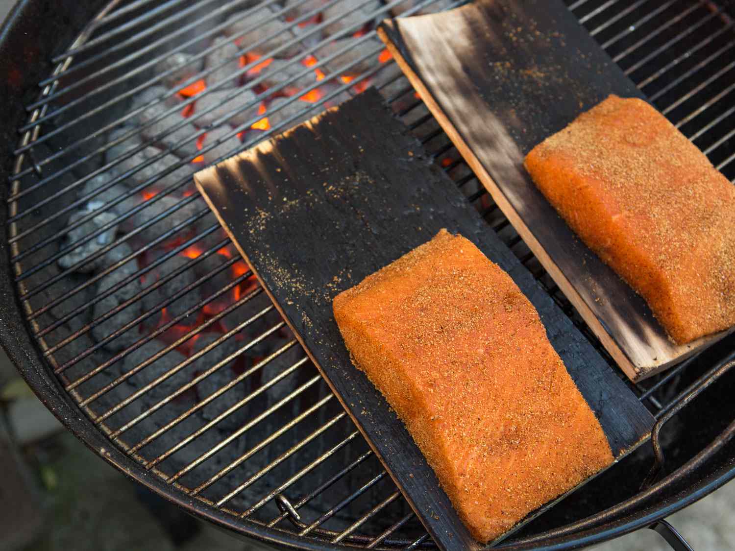 Two pieces of seasoned salmon on charred grilling planks on a hot grill.