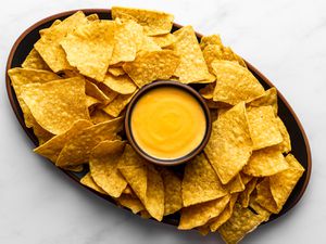 Nacho cheese sauce in a small bowl in the center of a platter, surrounded by tortilla chips.