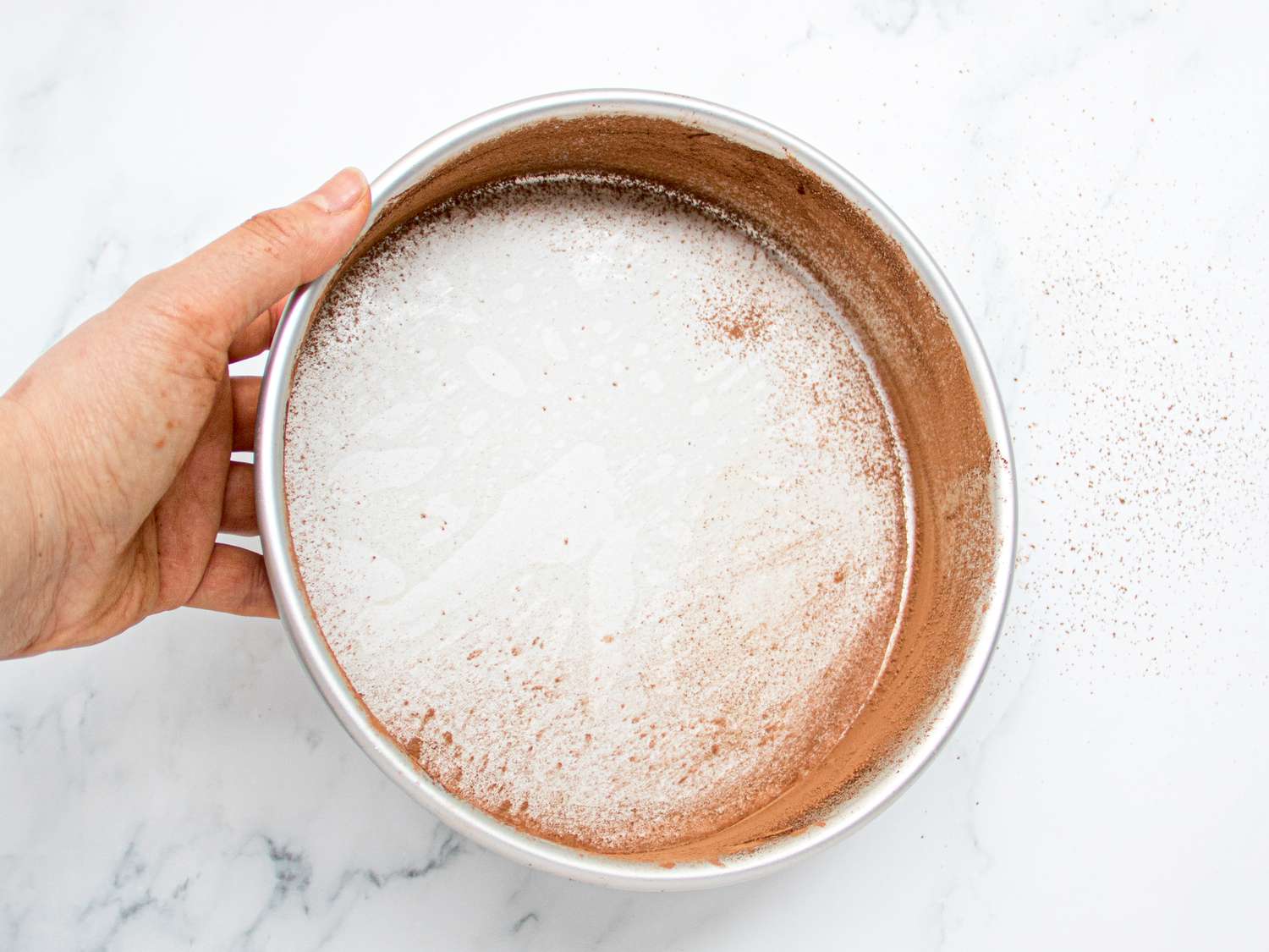 Overhead view of dusting cake pan with cocoa powder