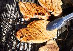 Chicken breasts cooking on a grill with tongs holding one piece