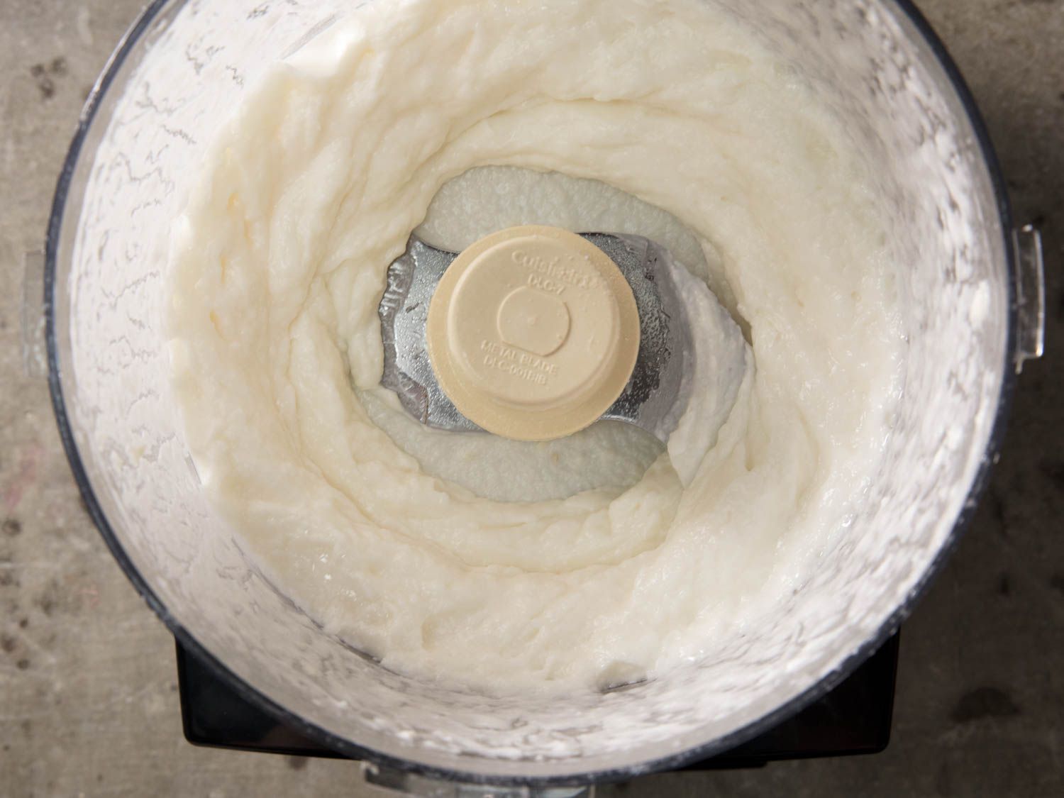 Overhead view of toum in food processor; the garlic has been processed to become a smooth puree.