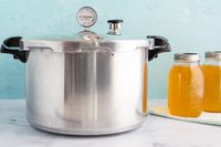 Presto 16-Quart Pressure Canner and Cooker On a counter next to two mason jars of broth