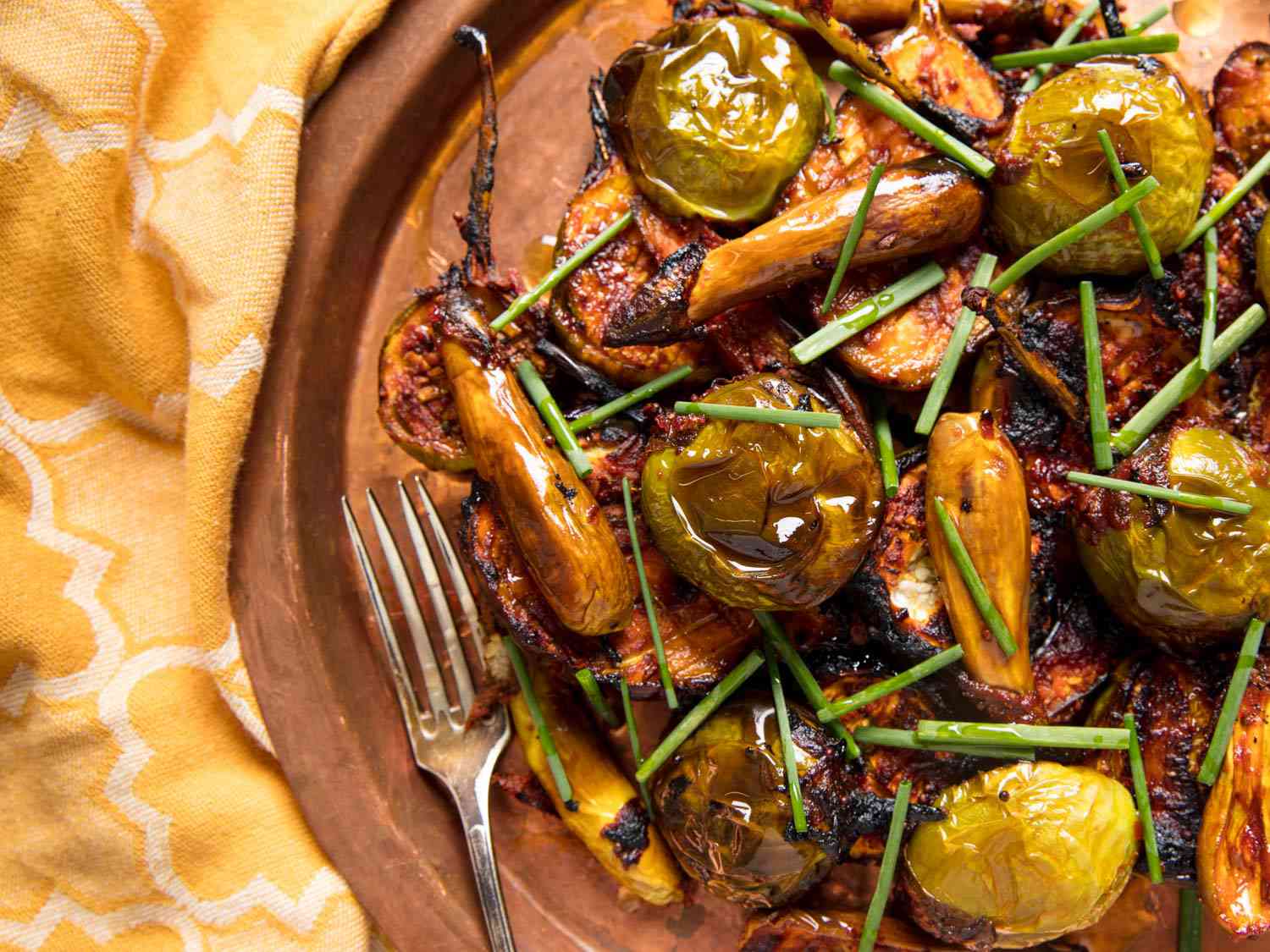 A close-up overhead view of spiced eggplant with mustard seeds on a yellow linen.