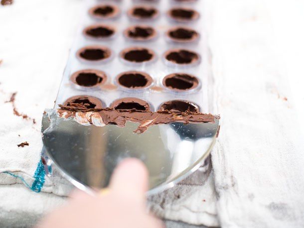 Using a metal scraper to completely scrape the top of the bonbon mold of any extra chocolate.