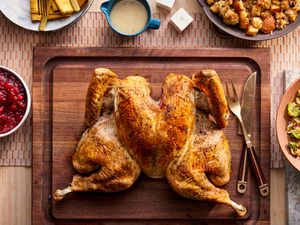 Spatchcocked Turkey on a wooden carving board surrounded by Thanksgiving dishes