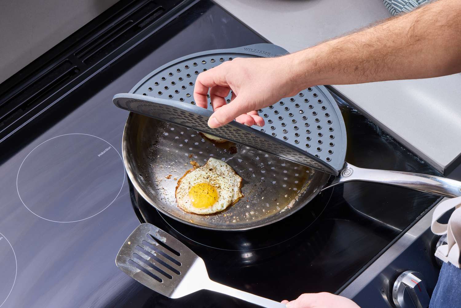 a person opening the williams sonoma splatter screen over a skillet with fried eggs