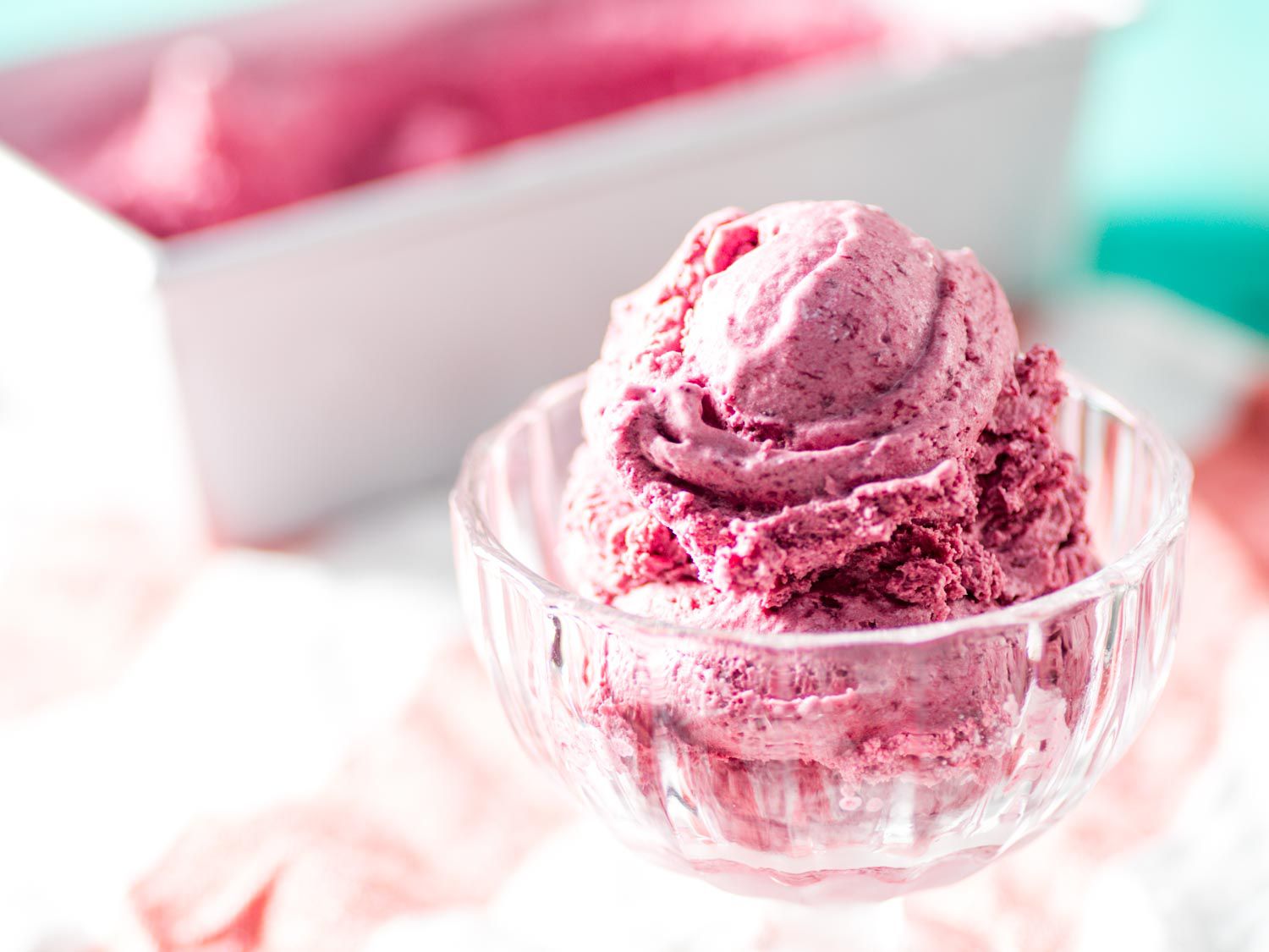 Cherry ice cream in a glass dish, container of ice cream out of focus behind it.
