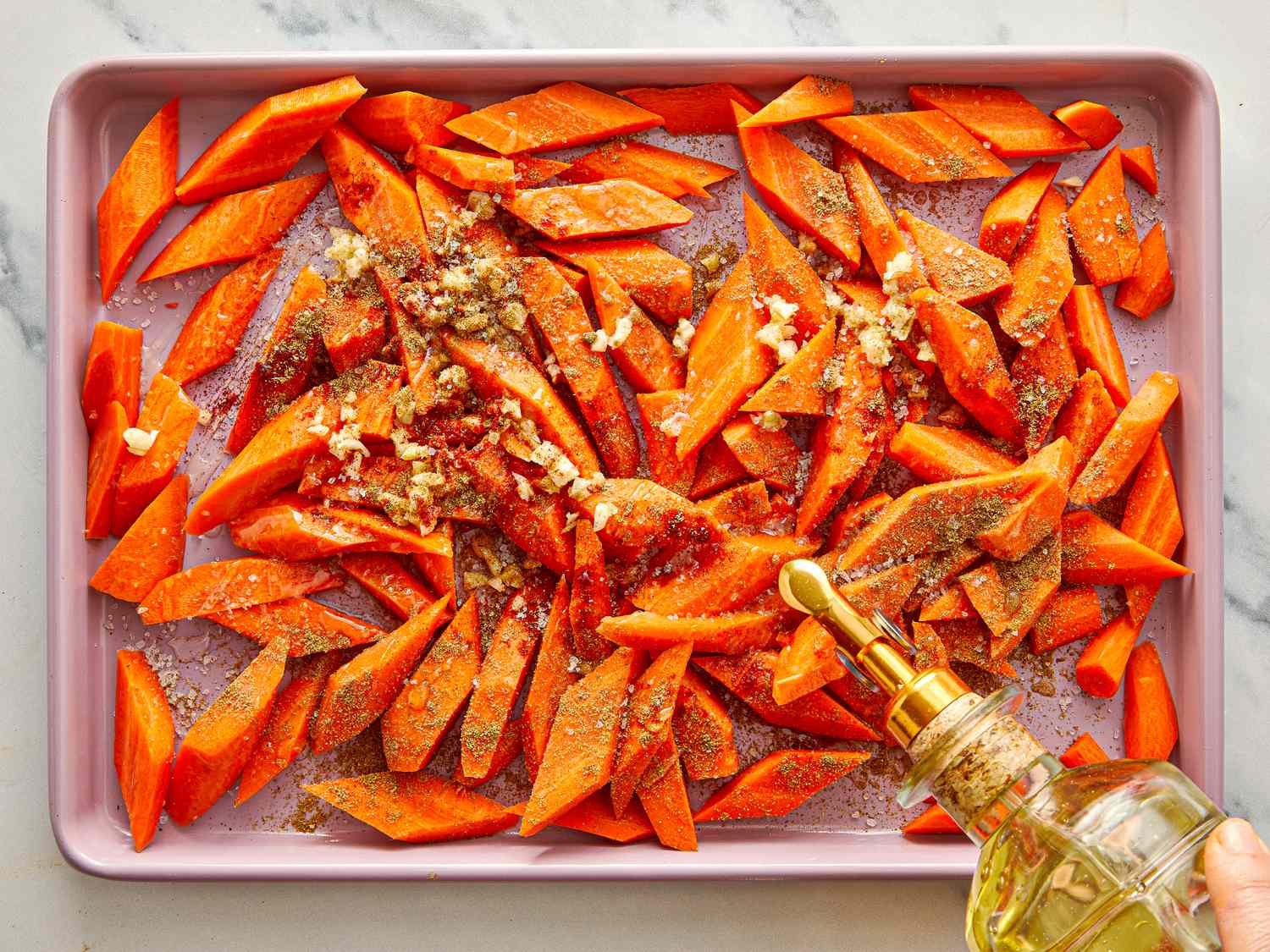 Chopped carrots on a baking tray being drizzled with oil and seasoned