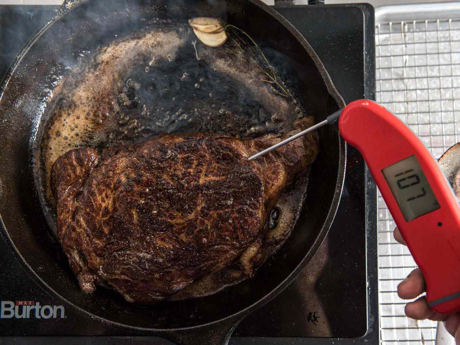 Taking the temperature of a steak cooking in a cast iron pan