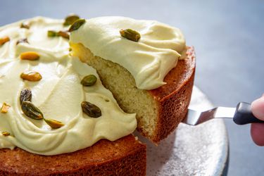 Closeup of a slice of pistachio cake being lifted with an offset spatula. The cake is generously slathered with homemade pistachio cream and dotted with whole pistachios.