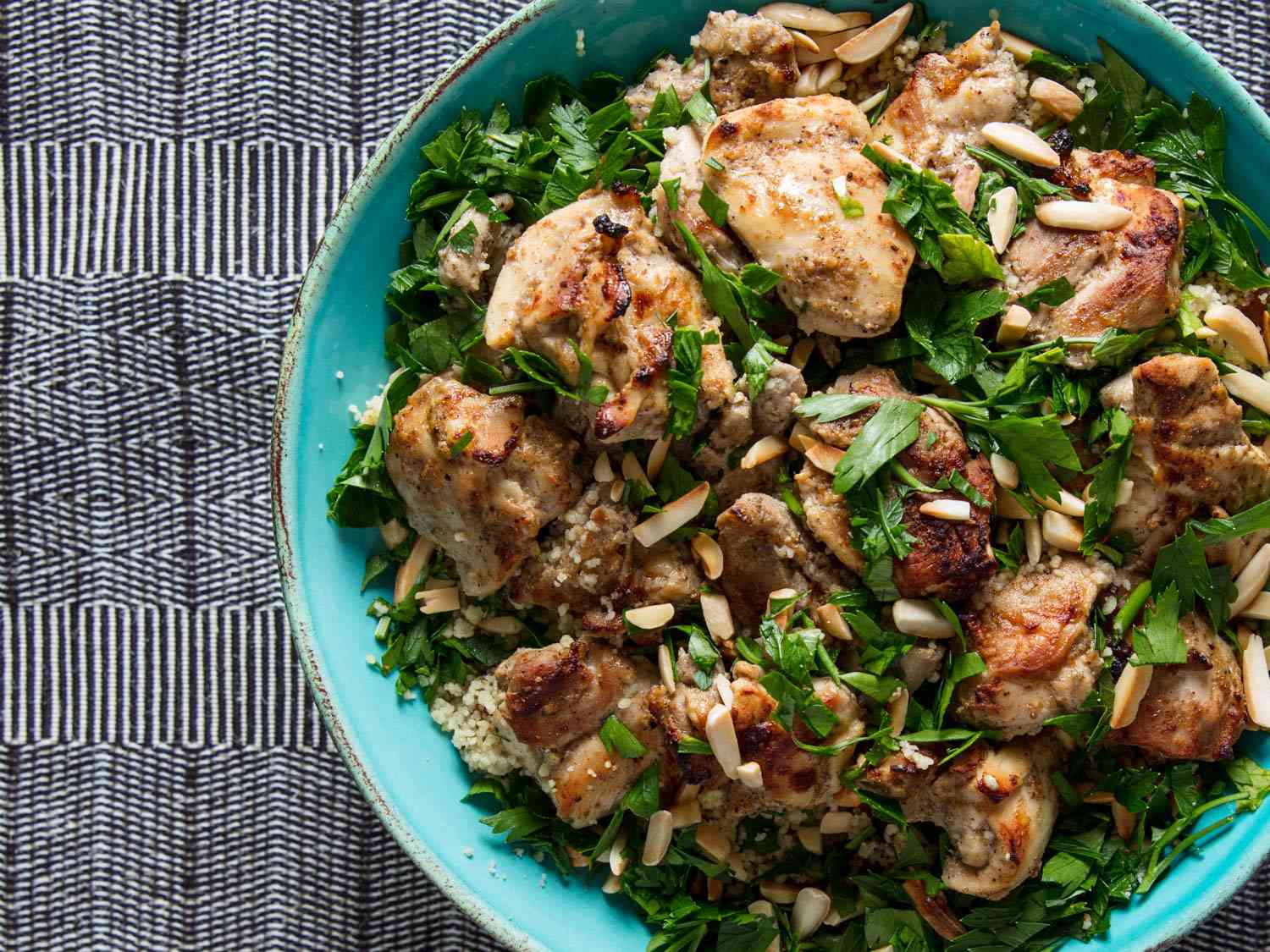 A bowl of tandoori chicken on couscous topped with fresh herbs and slivered almonds