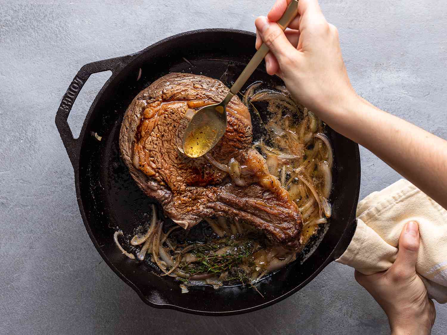 The steak in a cast iron pan with aromatics, being based with butter.