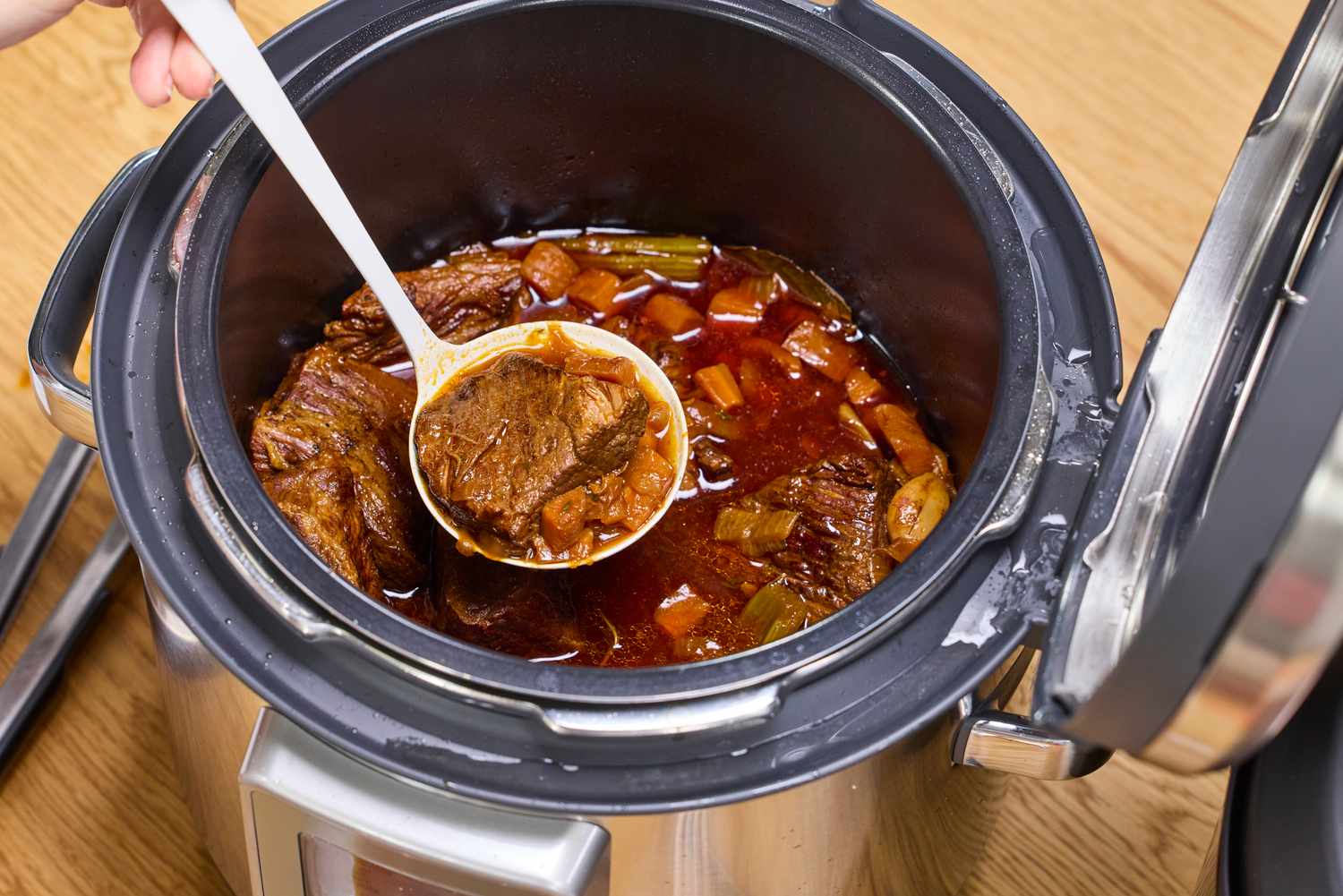 A person spoons cooked meat and vegetables from the Breville the Fast Slow Pro