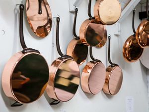 Copper pans hanging from hooks on white wall
