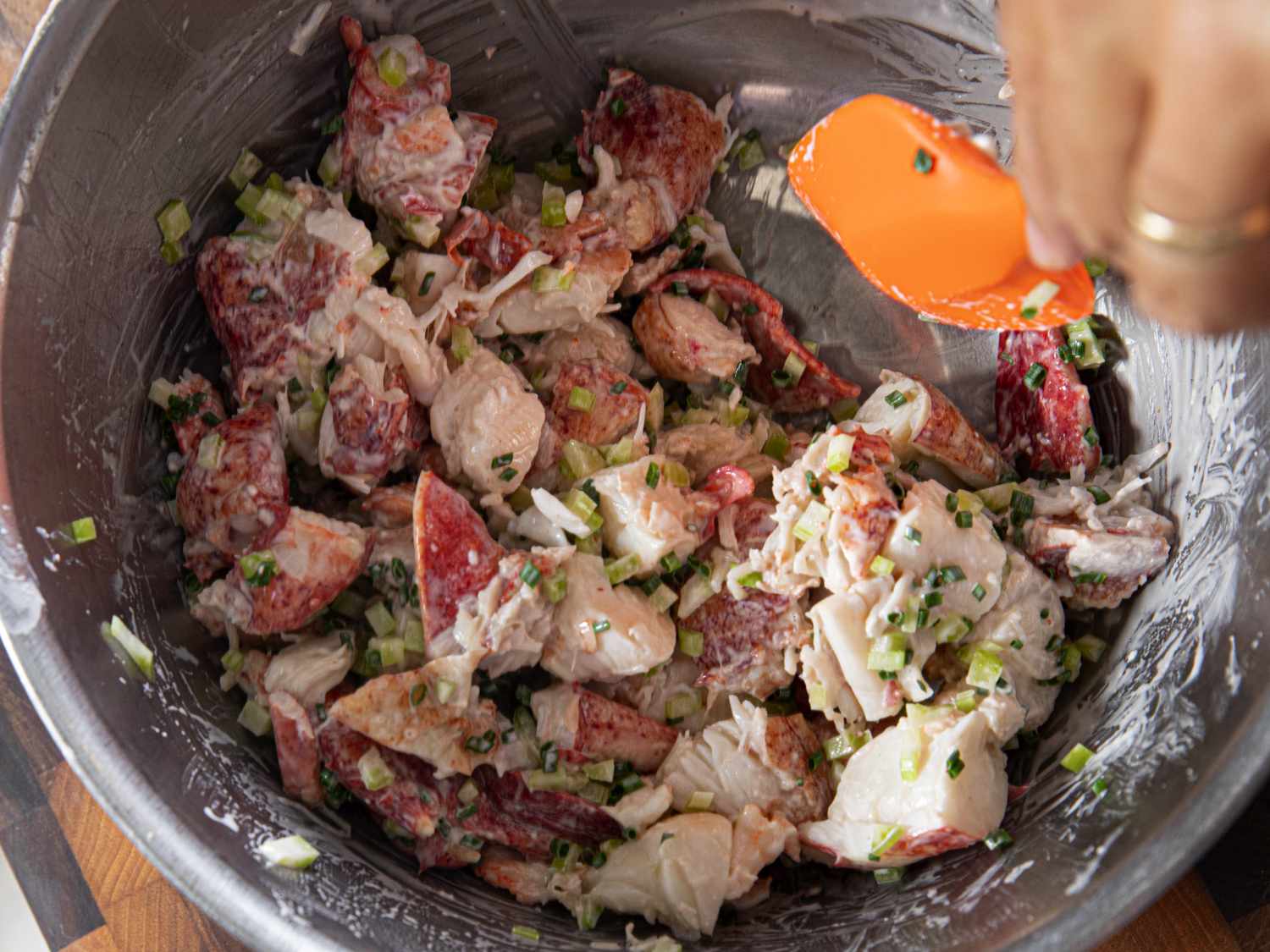Lobster meat being mixed with chives and mayo in a metal bowl